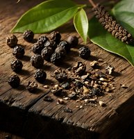 Black peppercorns with green leaves on rustic wooden surface, whole and crushed spices for culinary cooking and seasoning applications.