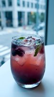 Berry mocktail with fresh mint and ice in a stemless glass by a window, vibrant red-purple hues, refreshing summer drink concept.