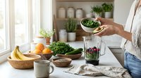 Woman preparing healthy green smoothie with fresh spinach in modern kitchen with natural ingredients and plants on counter for wellness lifestyle.