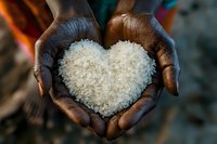 African hands holding white rice grains arranged in heart shape, symbolizing food charity, love, and care for humanity. Close up view against dark background.