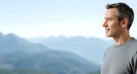 Middle-aged Caucasian male in casual gray shirt gazing at mountain landscape, expressing contemplation and peaceful solitude for wellness and lifestyle concepts.