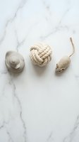 Cat toys collection on white marble surface featuring rubber ball, rope knot and plush mouse for pet entertainment and play activities.