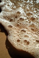 Foamy sea waves with bubbles washing onto sandy beach shore creating natural texture and patterns for coastal and marine themed designs.