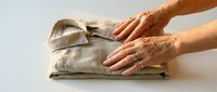 Mature woman's hands folding clean linen fabric on white surface, domestic chore and household laundry care concept for home organization and cleaning services.
