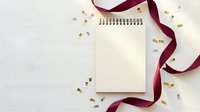 Blank spiral notepad with burgundy ribbon and golden confetti on white background for celebration planning and festive note-taking.