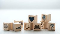 Wooden blocks with various symbols including heart, brain, scales of justice, lotus flower and question marks arranged on white surface for concept design.
