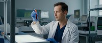 Middle-aged Caucasian male scientist in white lab coat examining test tube sample in modern research laboratory for medical analysis and scientific discovery.