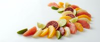 Fresh citrus fruit slices arranged in curved line on white background. Colorful orange, grapefruit, lime and lemon segments with mint leaves for healthy eating.