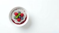 Acai bowl topped with powdered sugar, fresh raspberries, blueberries, and mint leaves on white background. Healthy breakfast.