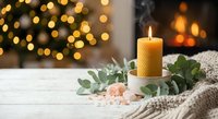 Cozy winter home decor with burning candle, eucalyptus leaves and warm bokeh lights creating peaceful holiday atmosphere for relaxation and wellness.