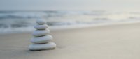 Zen stone stack on sandy beach with soft ocean waves in background creating peaceful meditation and mindfulness atmosphere for wellness and relaxation concepts.