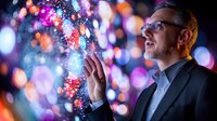 Caucasian businessman in glasses and suit jacket reaches toward magical glowing bokeh lights and sparkles against dark background with colorful illumination.