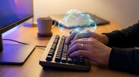 Cloud computing technology concept with businessman hands typing on keyboard and holographic cloud icon floating above workspace.