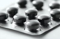 Close-up macro shot of black round pills in blister pack on white background, selective focus on medicine capsules with soft blur effect. Medical concept.