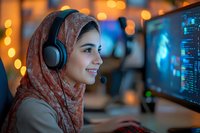 Young woman in hijab wearing headphones smiles while working at computer with bokeh lights in background, representing modern workplace diversity and remote work culture.