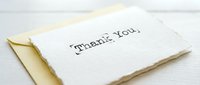 Handwritten thank you card with yellow envelope on white wooden surface, expressing gratitude for gifts, events, or personal messages.
