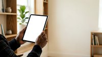 Senior African American man holding tablet with blank screen in modern home office with wooden shelves and potted plant, suitable for technology and business applications.