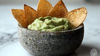 Fresh guacamole dip served in rustic stone bowl with crispy tortilla chips arranged in fan pattern, perfect for appetizers or party snacks.