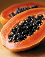 Fresh ripe papaya cut in half showing juicy orange flesh and black seeds on wooden surface, macro close up view for food photography and healthy eating.