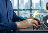 Professional businessman typing on laptop with glowing percentage discount icons floating around hands in modern office environment for e-commerce sales.