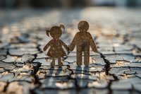 Rustic wooden figures of boy and girl holding hands stand on cracked earth surface, symbolizing childhood friendship, environmental concerns and drought conditions.