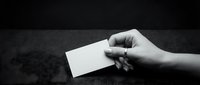 Hand holding a blank white business card on a dark textured surface, monochrome style, copy space for branding or contact details.