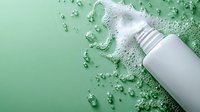 White cosmetic bottle with pump dispenser surrounded by water droplets and splash on mint green background for skincare product advertising.