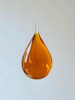 Golden amber liquid drop suspended in mid-air against light background, showcasing viscosity and surface tension in minimalist composition.