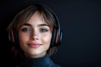 Young woman with headphones smiling warmly in cozy sweater against dark background for music streaming and audio entertainment content.