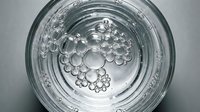 Clear glass with water bubbles floating on surface creating abstract circular patterns for refreshing beverage and hydration concepts.