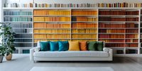 Modern living room interior with rainbow colored book collection on built-in shelves, gray sofa with colorful cushions and decorative plant creating cozy reading space.