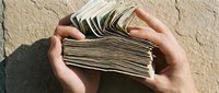Hands holding stack of cash money outdoors in sunlight, representing wealth, savings, financial success, income, and business earnings for commercial use.