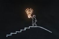 Glowing lightbulb held by chalk-drawn figure climbing stairs on blackboard, representing innovation, growth, and creative problem solving in business concept.