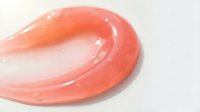 Glossy coral pink lip gloss swirl on white background, cosmetic texture for beauty and makeup applications.