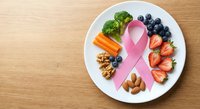 Healthy nutrition concept with pink ribbon symbol for breast cancer awareness surrounded by nutritious foods including broccoli berries nuts on white plate.