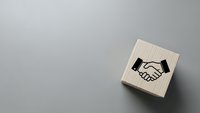 Wooden rubber stamp with handshake icon on gray background for business partnership and agreement concepts in office branding materials.
