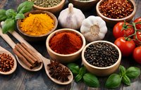 Colorful spices and herbs in wooden bowls with fresh vegetables on rustic table for cooking and seasoning culinary preparations.