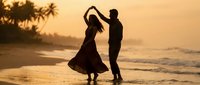 Romantic couple dancing on tropical beach at sunset with palm trees and ocean waves creating silhouette against golden sky for vacation romance concept.