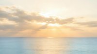 Serene ocean sunrise with golden sunlight breaking through soft clouds over calm turquoise waters, creating a peaceful coastal seascape for relaxation and travel themes.
