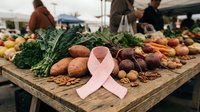 Fresh organic vegetables and fruits displayed at farmers market with pink breast cancer awareness ribbon symbolizing healthy nutrition for disease prevention.