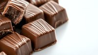 Milk chocolate candy pieces with decorative striped pattern on white background, close-up macro shot showing rich texture and glossy surface of gourmet confectionery.
