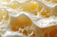 Frothy white foam with golden bubbles in macro photography shows delicate texture and light patterns creating abstract background for beverage designs.