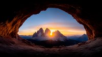 Dramatic sunrise view through natural rock arch framing Tre Cime di Lavaredo peaks in Dolomites, orange sky and mountain silhouettes creating mystical atmosphere.