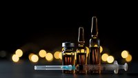 Medical glass vials with amber liquid and syringe on dark background with warm bokeh lights for healthcare and pharmaceutical concepts.