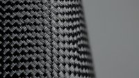 Carbon fiber weave texture with detailed macro view showing interlaced black fibers in geometric pattern for industrial and automotive design applications.