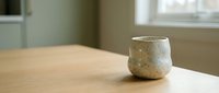 Ceramic cup with textured glaze sitting on wooden table in bright interior space, suitable for home decor, lifestyle, and product photography projects.