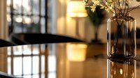 Elegant glass vase with delicate white flowers on reflective surface, warm ambient lighting creates cozy atmosphere in modern interior setting.