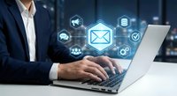 Professional businessman typing on laptop with glowing email and digital communication icons floating above keyboard in modern office environment.