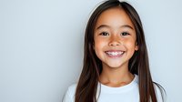 Young Asian girl with braces showing bright cheerful smile against light background. Natural lighting highlights genuine expression and long dark hair.