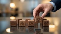 Businessman hand placing wooden blocks with business icons representing strategic planning and corporate development in modern office environment.